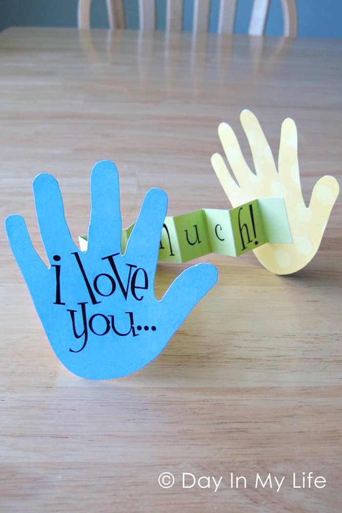 i love you this much, written with black, on two paper cutouts, shaped like child's hands, connected with green piece of folding paper