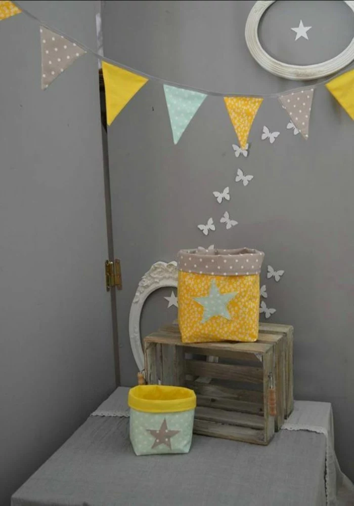 garland with patterned triangular flags, in yellow and light blue and gray, near wooden crate, and two fabric pouches, on table covered in gray fabric, dark gray kitchen or dining room