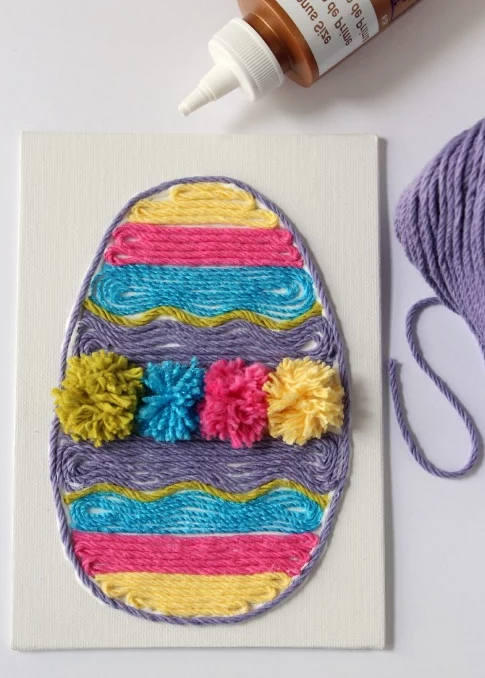 colorful egg collage on white card, shaped like an egg, easter crafts for adults, decorated with yellow, pink and blue pom poms and thread