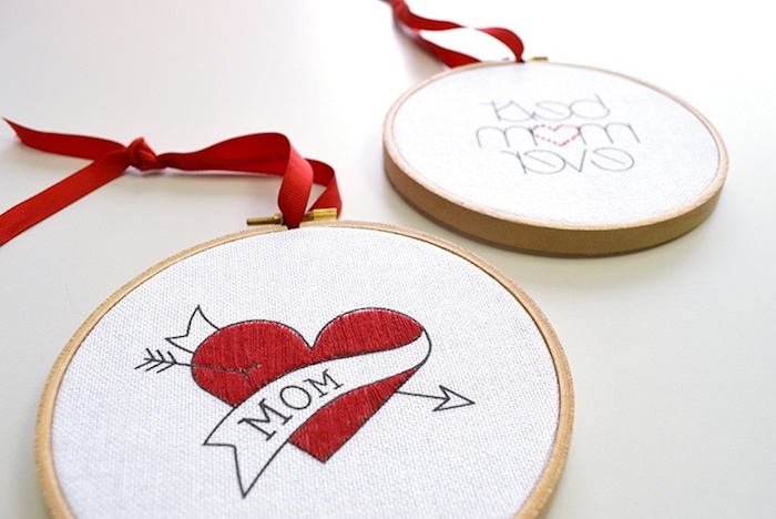close up of two round, white peaces of cloth, embroidered with red and black thread, with hearts and messages for mom, top 10 mother's day gift ideas, with red ribbons