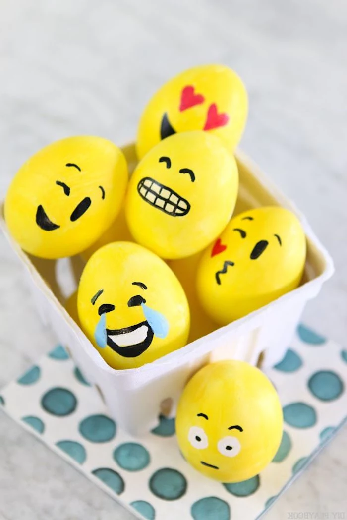 different funny faces or emojis, on easter eggs, painted in yellow, decorated with black, red and white paint, easter crafts for adults, inside white ceramic dish