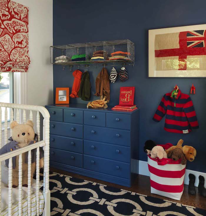 striped red and blue child's jumper, hanging on dark blue wall, with matching chest of drawers, white crib and teddy bear, boys room ideas