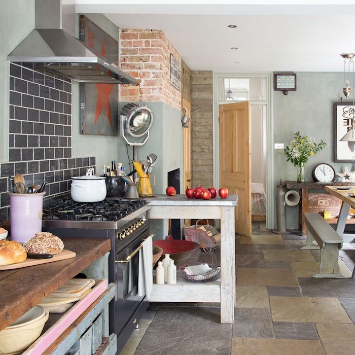 country kitchen décor, floor with brown and beige stone tiles, pale gray walls with brickwork details, shabby chic wooden counters, and an antique stove