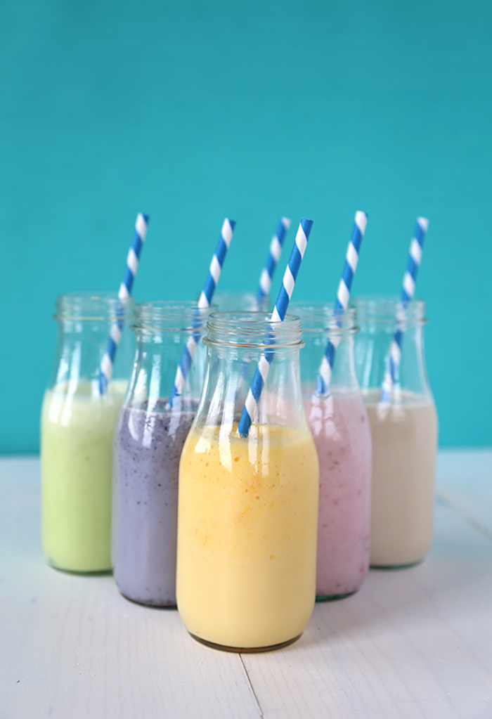 fruit milk in different colors, poured in five bottles, each decorated with a striped straw, easy smoothie recipes, green and purple, yellow and pink