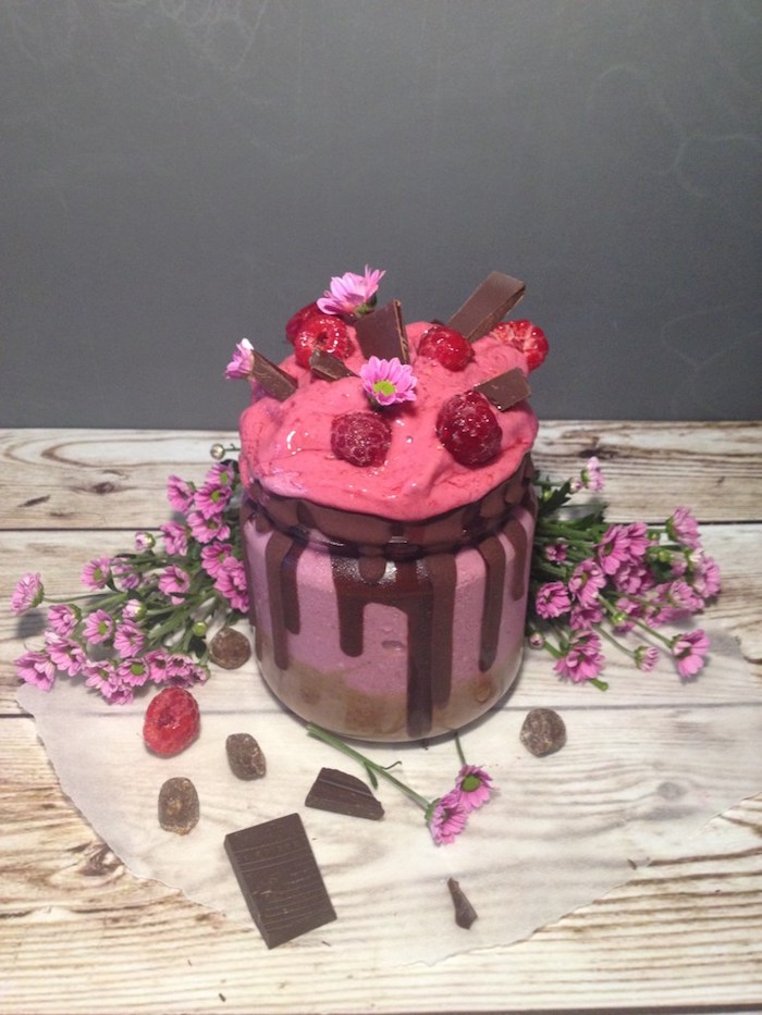 milk chocolate pieces, raspberries and small flowers, topping a pink creamy dessert, how to make a fruit smoothie, more flowers and berries nearby