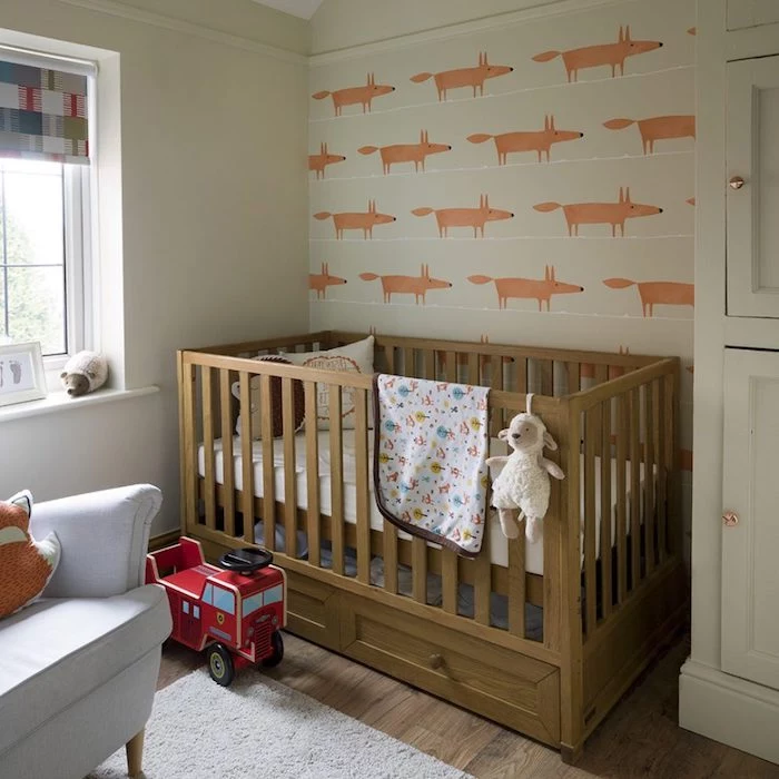 simple baby room, minimalist nursery ideas, off-white wallpaper with fox pattern, brown wooden crib, red fire-engine toy, and stuffed lamb doll