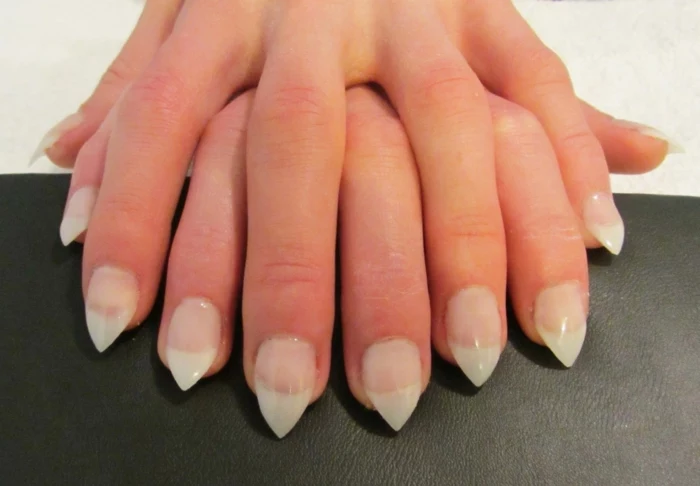 two hands placed on top of each other, with sharp stiletto nails, nude pink bottom part, and white tips, french manicure style