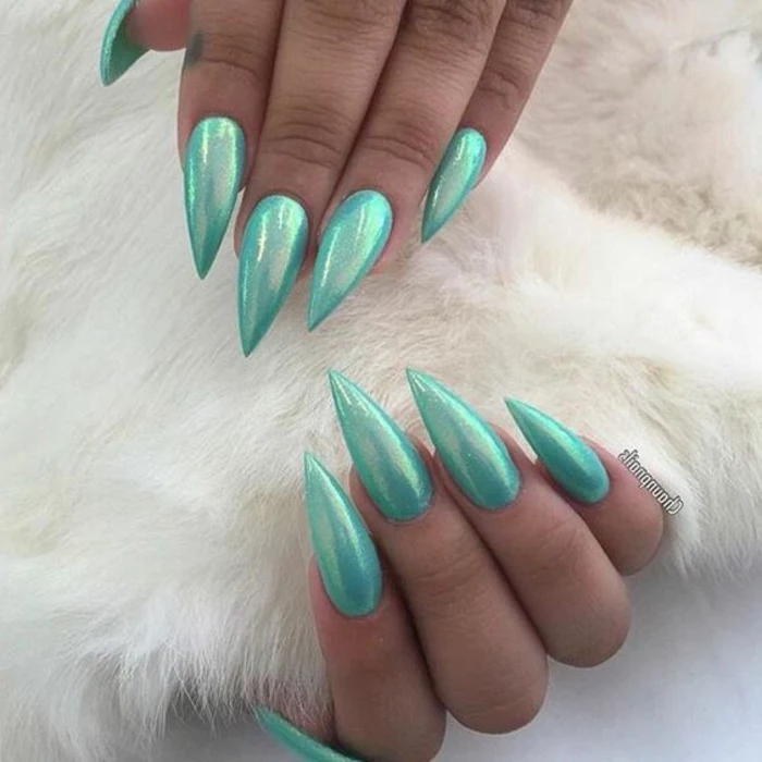 mermaid stiletto nails, long and sharp, painted in iridescent, teal blue nail polish, on two hands, holding soft white fur