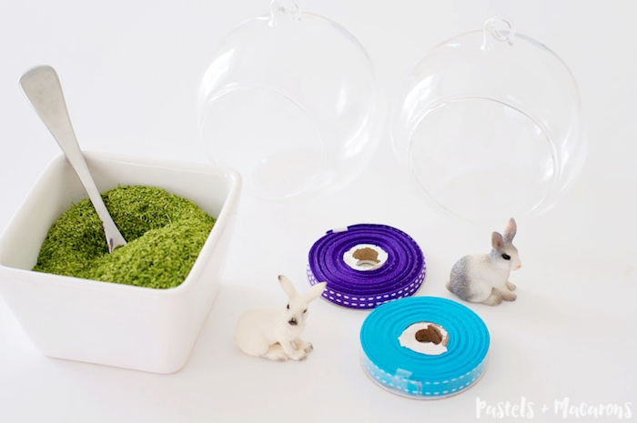 terrariums made of glass, near white dish, filled with moss, easter projects, rolls of pale blue and purple ribbon, and two realistic rabbit figurines