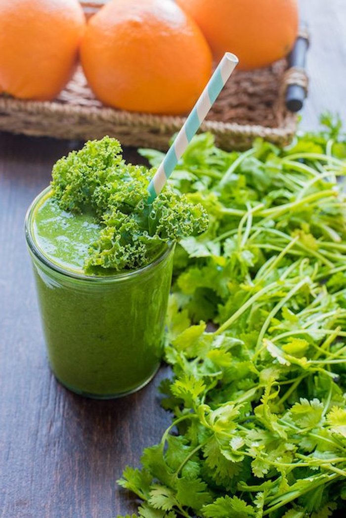 kale and spinach smoothie, with blended parsley, in a clear glass, decorated with kale leaf and straw, oranges in background