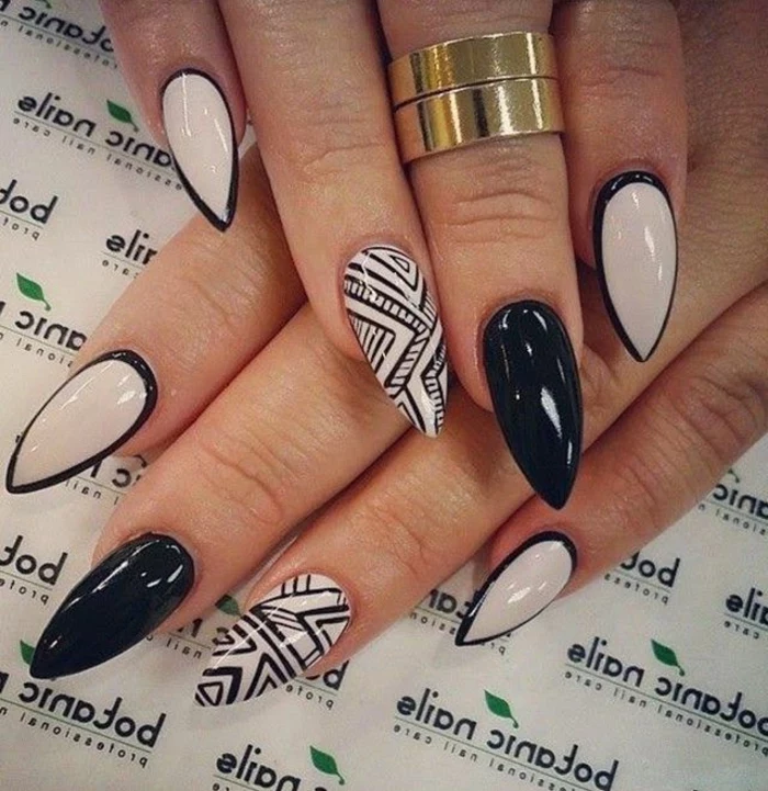 contasting white and black stiletto nails, black hand-drawn details, and frame effect, on two hands, with solid gold rings