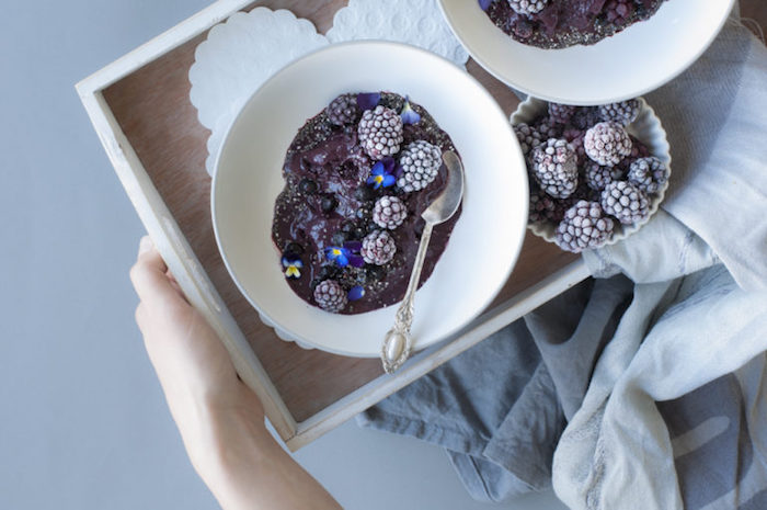 tray with two bowls, containing blended fruits, decorated with frozen blackberries, and tiny blue flowers, healthy breakfast smoothies, small dish with more frozen blackberries