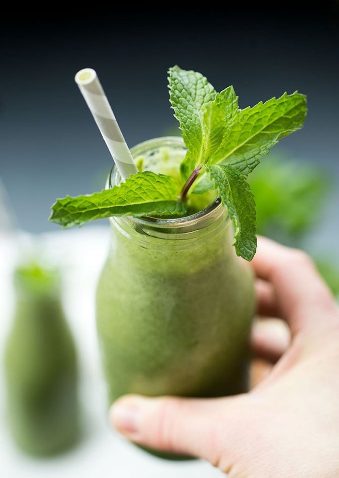 fresh spearmint stalk, inside a small bottle, green smoothie recipe, filled with a green blended drink, and held by a human hand