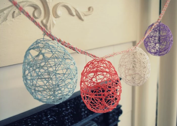 meshy and hollow, egg-shaped decorations, easter arts and crafts, made using balloons, glue and thread, hanging on a colorful rope, near a fireplace