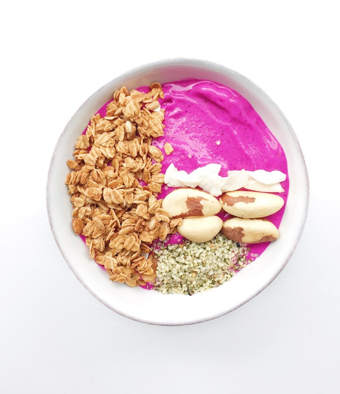 brazil nuts and seeds, cream and oatmeal, topping a hot pink smoothie, made from blended beets, in a white bowl