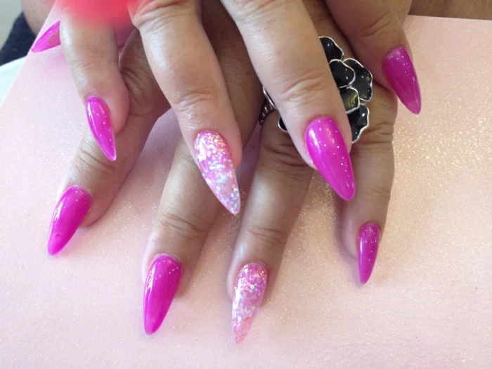 massive flower-shaped metal ring, on hand with long claw nails, in hot pink nail polish, decorated with light pink, and silver glitter