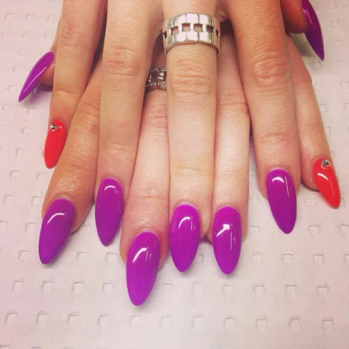 bright purple and red nails, smooth and long manicure, decorated with a few rhinestone stickers, on hands with chunky silver rings