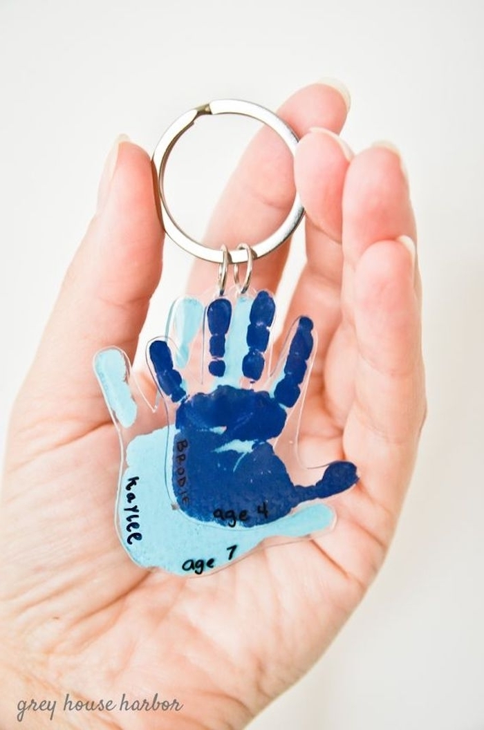navy and light blue baby hand prints, coated in clear plastic, and attached to a metal keyring, mother's day gifts for grandma, held by a person's hand