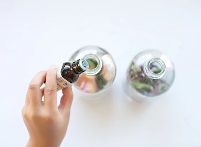 gift ideas for mom, child's hand pouring lavender essential oil, into clear glass bottles, filled with flowers