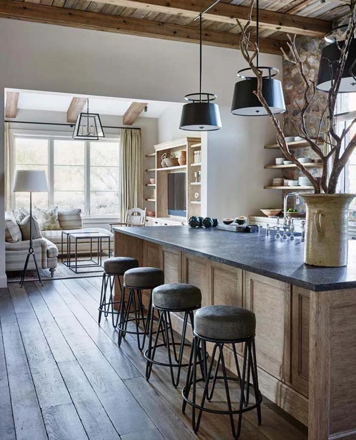 massive wooden floorboards, inside open plan kitchen, with large kitchen island, stone-covered walls with shelves, and decorative tree in a large ceramic vase