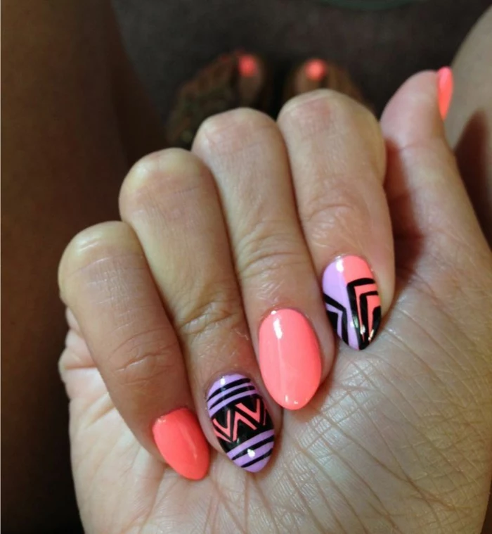 spring or summer manicure, with neon pink, and light purple nail polish, decorated with black, hand-drawn shapes, on short stiletto nails