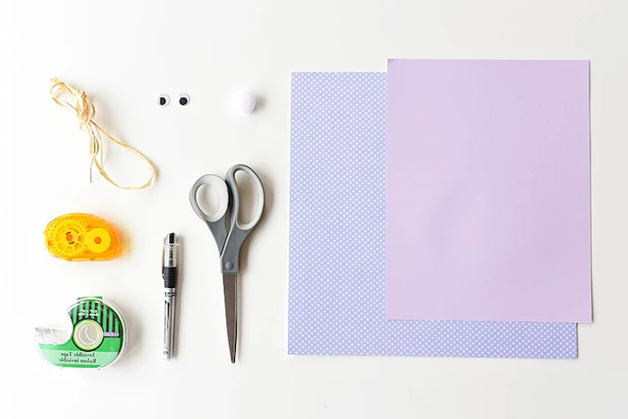 different kinds of stationary, scissors and a pen, two sticky tape dispensers, straw-like thread, eye stickers and a small cotton ball, craft ideas for kids, two sheets of plain, and patterned purple paper