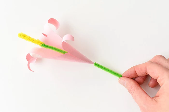 easter arts and crafts, a single pink lily, made from folded, and rolled paper, with green stalk, and yellow pistil, made from fuzzy wire