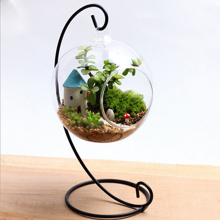 mushroom and house, tiny painted figurines, inside a hanging terrarium, made of glass, on a black metal stand, filled with succulents and moss