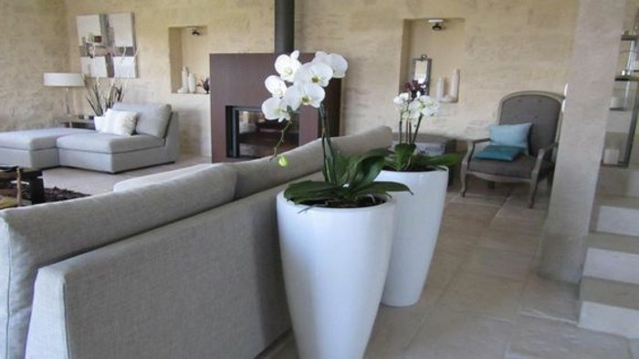 big ceramic vases in white, with planted white orchids, near light gray sofa, living room color ideas, spotty pale beige walls, dark brown fireplace
