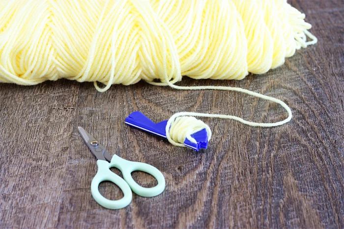 lots of pale yellow thread, some woven around a bright blue knitting tool, near pair of small light blue scissors, easter crafts for kids