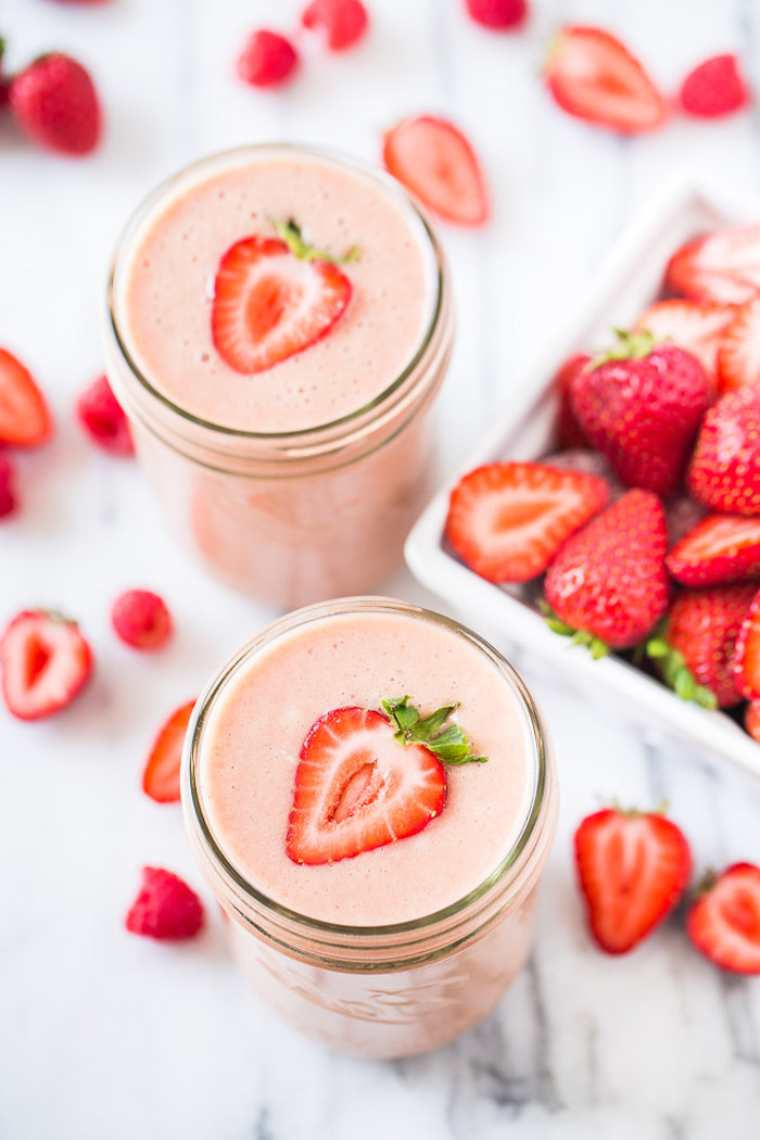 mason jars filled with pale pink, creamy and smooth drink, topped with halved strawberries, healthy smoothie recipes, more berries nearby