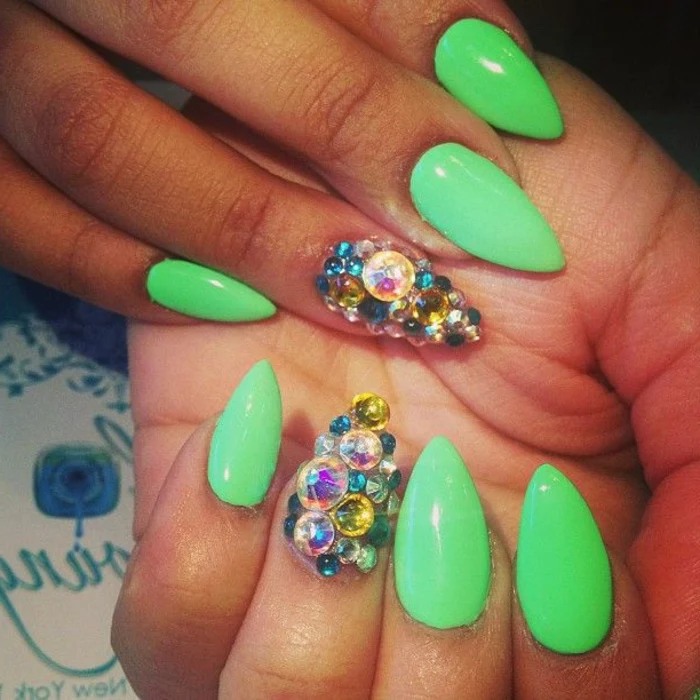 vibrant neon green nail polish, on oval sharp manicure, two of the nails are encrusted, in multicolored rhinestone gem stickers