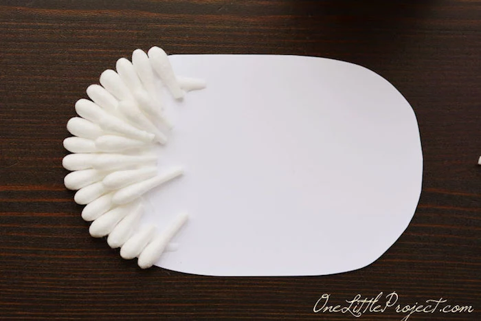 sticking cotton bud tips, on top of each other, on a white, oval piece of paper, resting on a dark wooden surface, easter crafts for kids, cute sheep idea