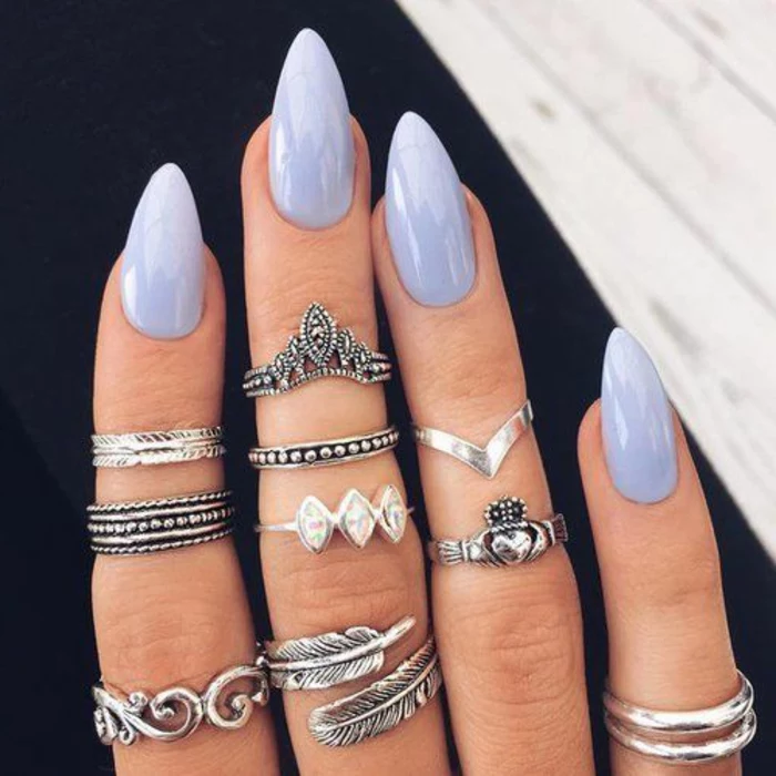 many boho-style decorative silver rings, on four fingers, painted in pale, milky violet nail polish