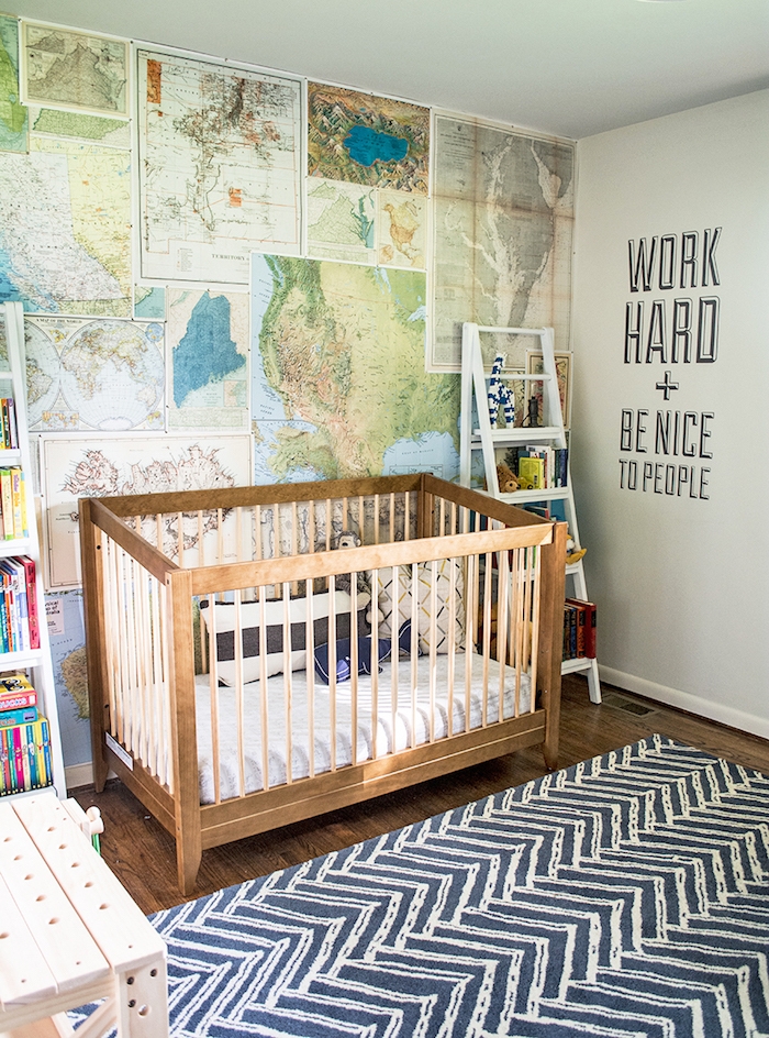 navy blue rug, with white pattern, in gender neutral nursery, one wall covered with different maps, wooden crib with white bedding