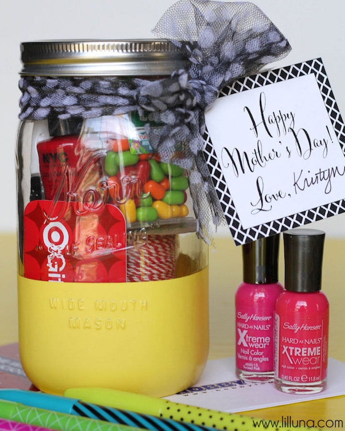 pens in different colors, and two bottles of nail polish, in cyclamen and red, near mason jar, half colored in yellow, containing mother's day goodies
