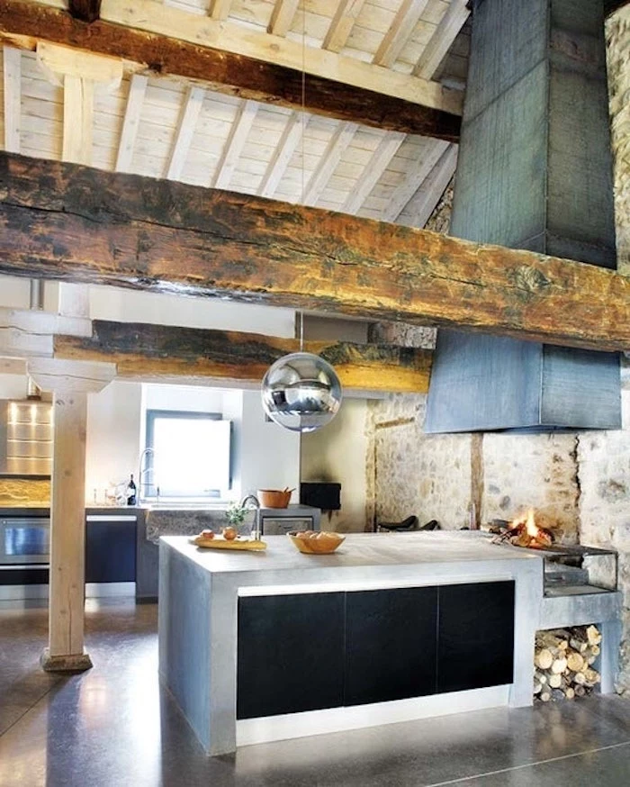 round metallic lamp, hanging from a vaulted ceiling, with wooden boards and beams, over an industrial style rustic kitchen, with fireplace and concrete kitchen island
