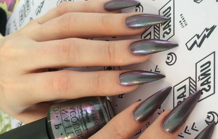 iridescent black nail polish, on long and sharp manicure, black stiletto nails, on two hands, holding a bottle of nail polish