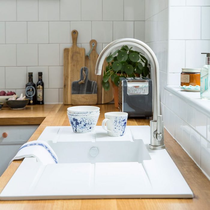 modern metal tap, on white sink, inbuilt in a light brown wooden counter, rustic country home décor, potted plant and several wooden cutting boards