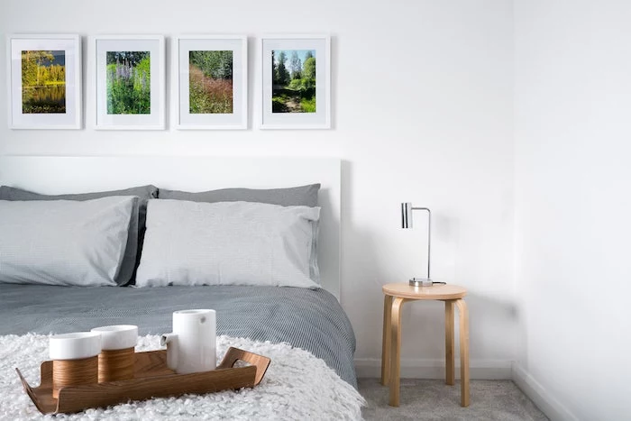 bed with covers in different shades of gray, four photographs in white frames, small wooden bedside table, colors that go with gray walls
