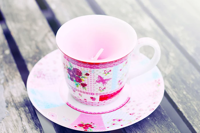 teacup with pink floral pattern, and matching saucer, containing light pink handmade candle, good mothers day gifts, rough wooden surface