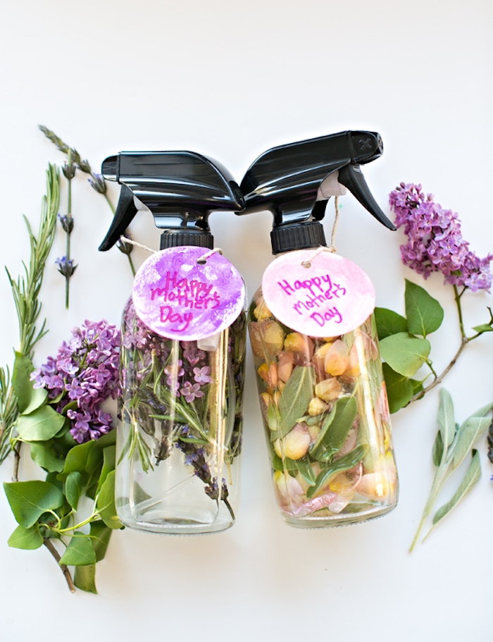 clear bottles with black, plastic spray caps, made from glass or plastic, filled with water and lilac, rose petals and herbs, mother's day gift ideas, fresh flowers nearby
