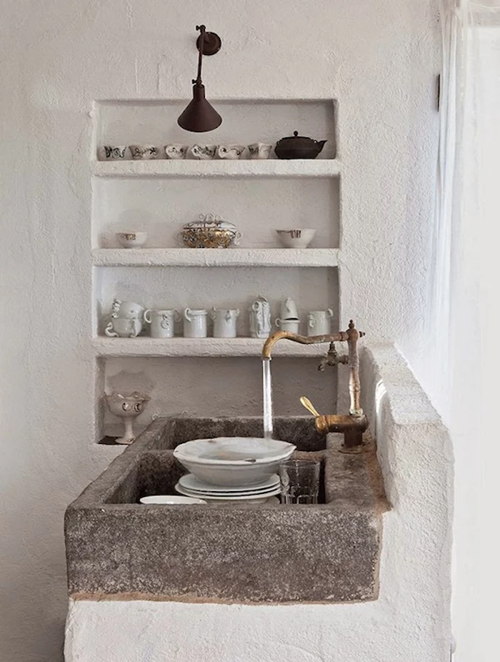 water from a brass antique tap, running over several dishes, inside a natural stone sink, rustic country home décor, lime plaster shelves, with cups and pitchers nearby