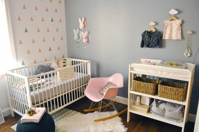 baby's nursery with blue grey paint on one wall, and light colored, patterned wallpaper on the other, pink rocking chair, various decorations in pink and gray
