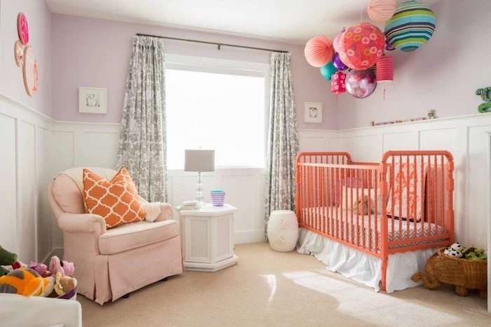 lots of multicolored paper lanterns, with different colors, shapes and sizes, hanging over orange baby crib, nursery ideas, pale orange armchair