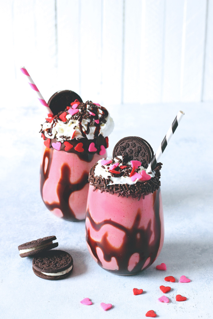 sugar hearts in pink and red, chocolate sprinkles, cream and oreo cookies, topping two tumbler glasses, filled with berry and chocolate blended drink, how to make a fruit smoothie, tasty dessert idea