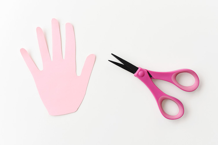 hand-shaped cutout, made from pale pink paper, easter diy, on white surface, near small pink scissors