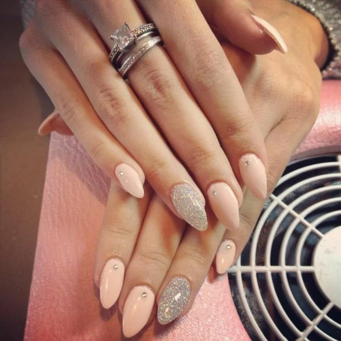 milky pastel pink, stiletto acrylic nails, decorated with small rhinestone stickers, and silver glitter