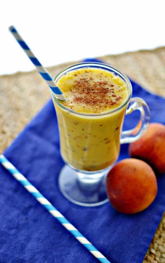 navy blue cloth, a straw and two peaches, clear glass with handle, containing yellow blended drink, dusted with brown powder, how to make a fruit smoothie