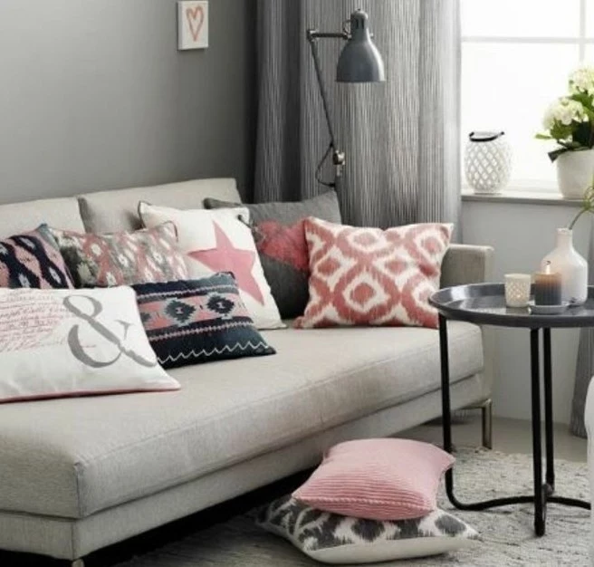 various cushions in pink, white and gray, on light gray sofa, near black metal coffee table, living room paint colors, grey walls and curtains